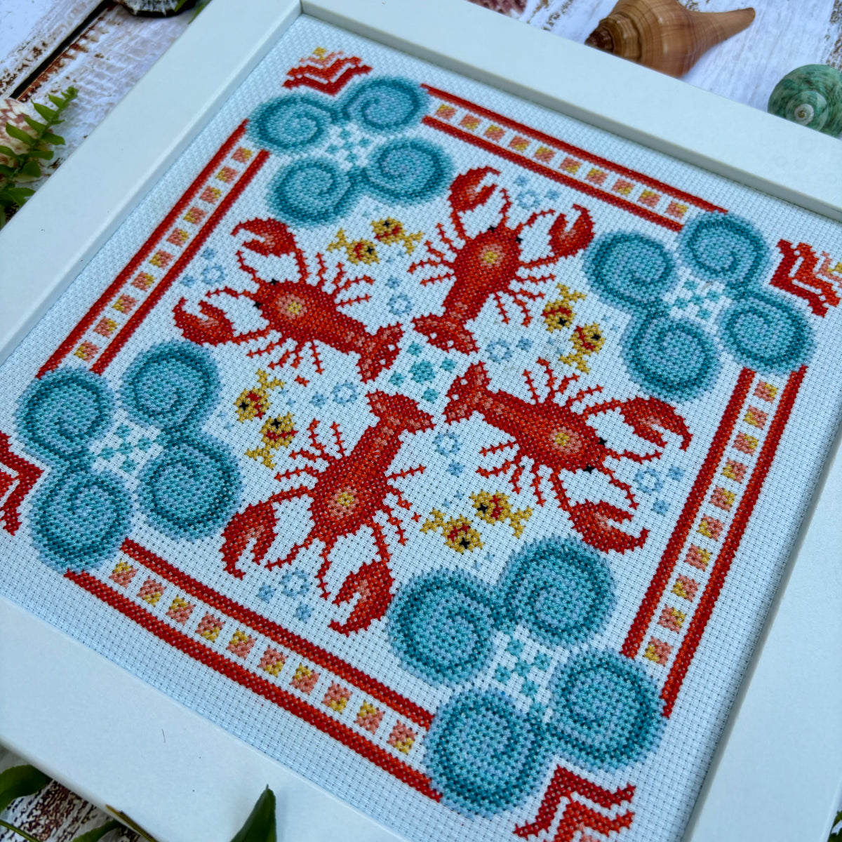 Cross-stitched pattern with red lobster and blue seafoam design on a white background