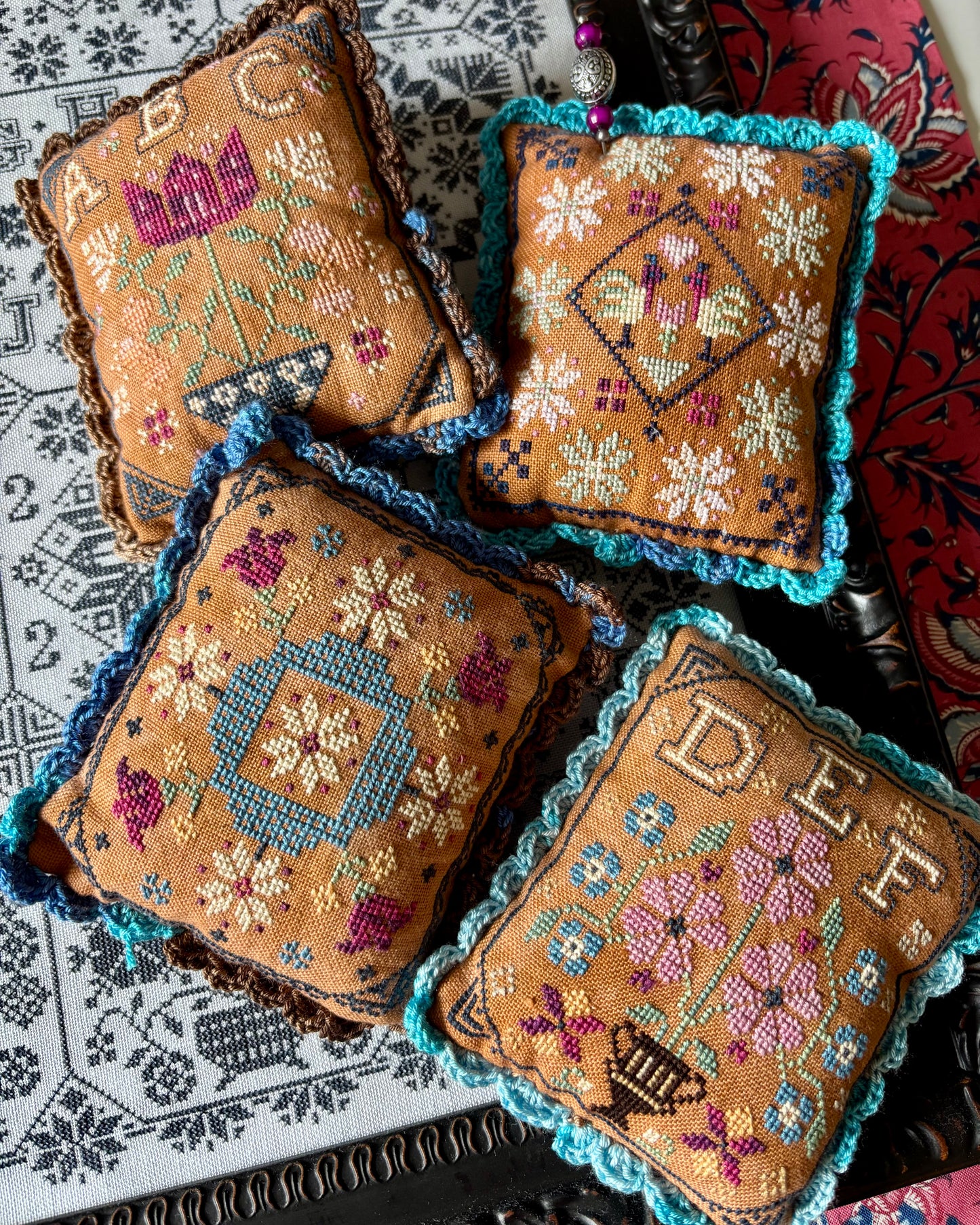 Four embroidered pillows with floral and geometric patterns on a textured surface.