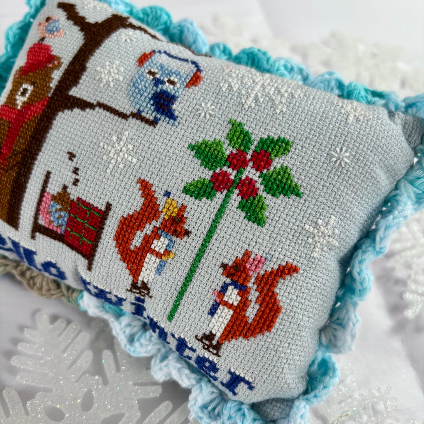 Decorative pillow with cross-stitched design of foxes and holly on a textured surface