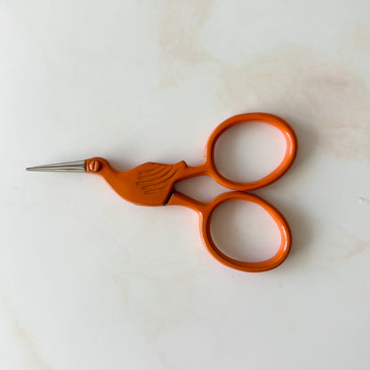 Pair of orange-handled scissors with bird design on a white background