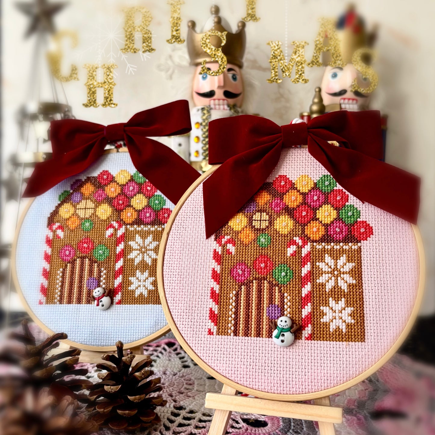 Two embroidered gingerbread houses with red bows on wooden stands, surrounded by Christmas decorations.