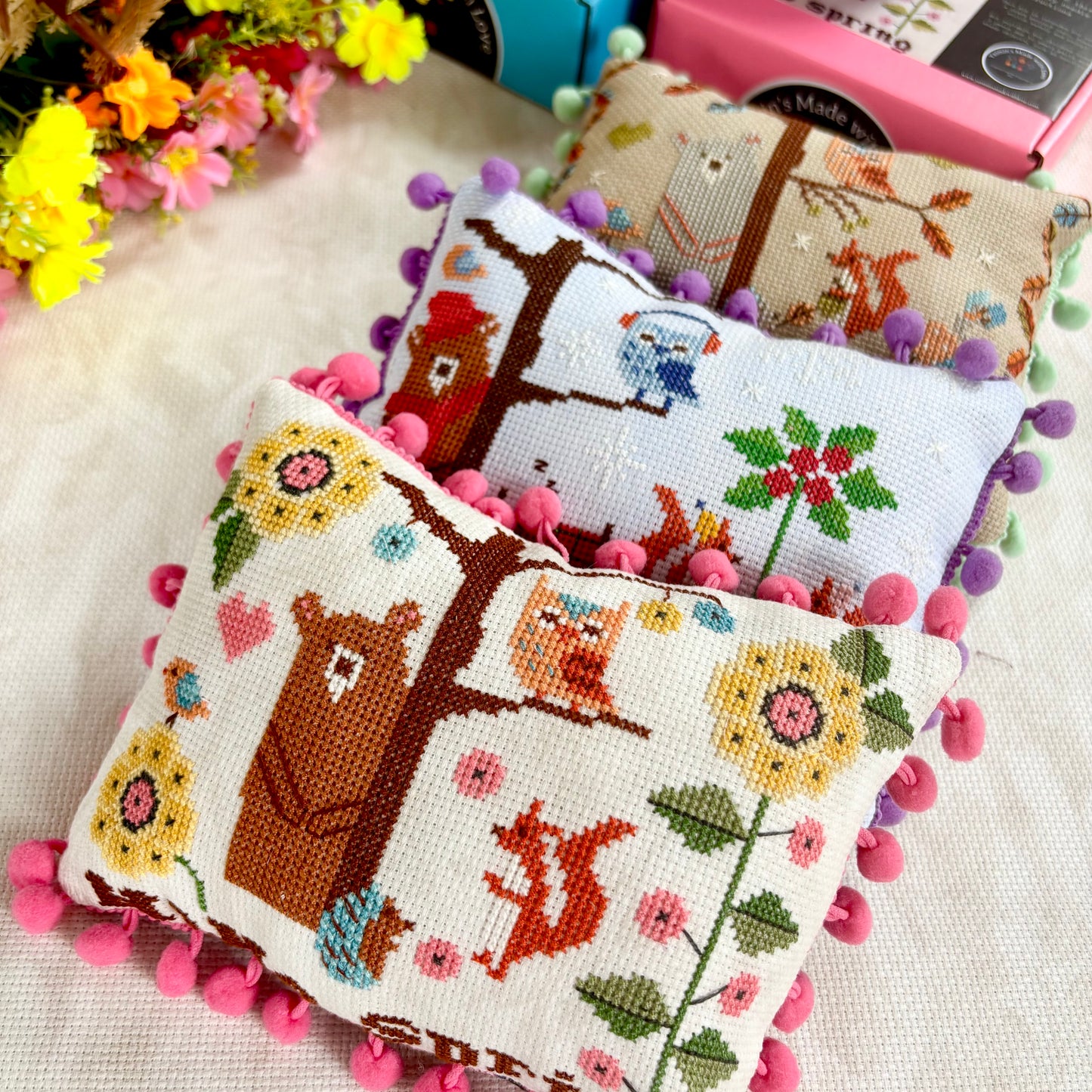 Cross-stitched cushions with animal and nature patterns on a textured surface.