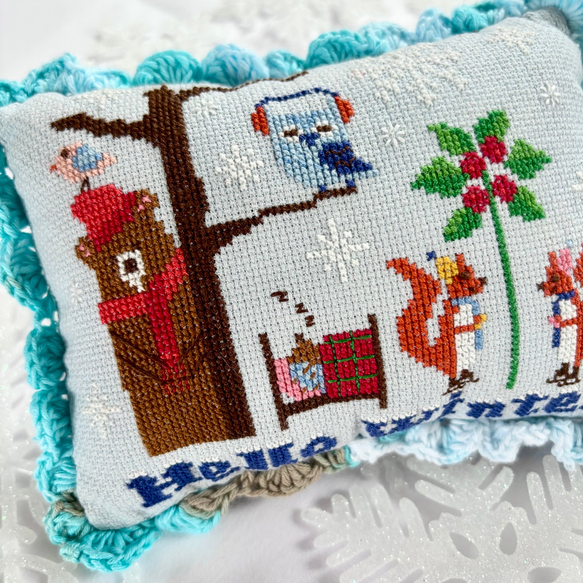 Cross-stitched pillow with animal-themed design on a textured surface