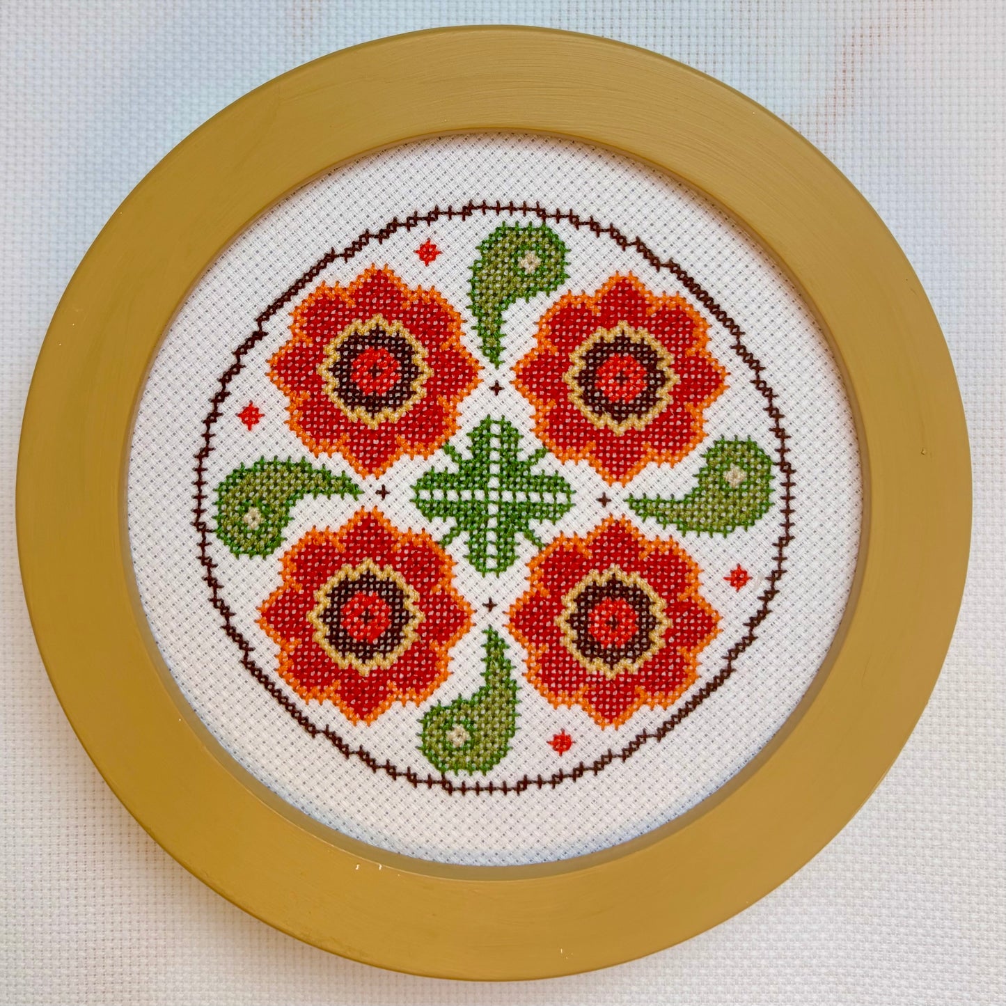 Circular cross-stitch pattern with red flowers and green leaves in a gold frame.