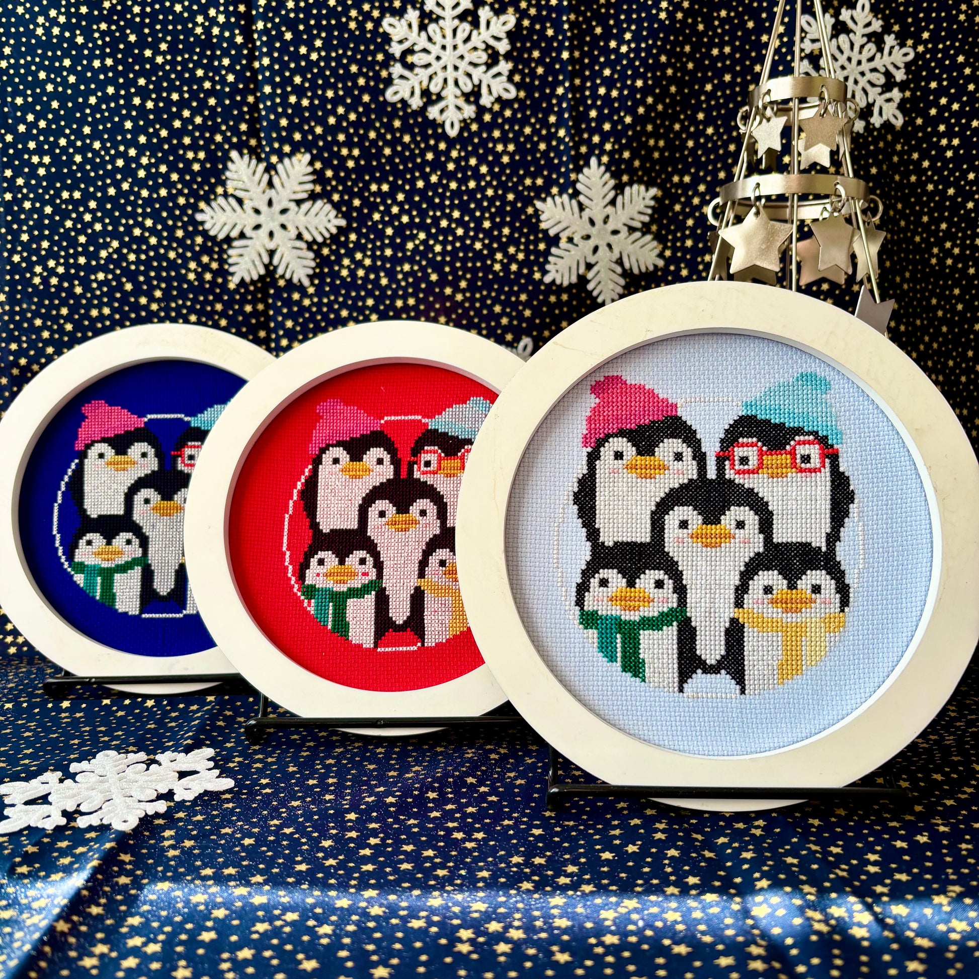 Set of cross-stitched penguin ornaments on a festive background with snowflakes.