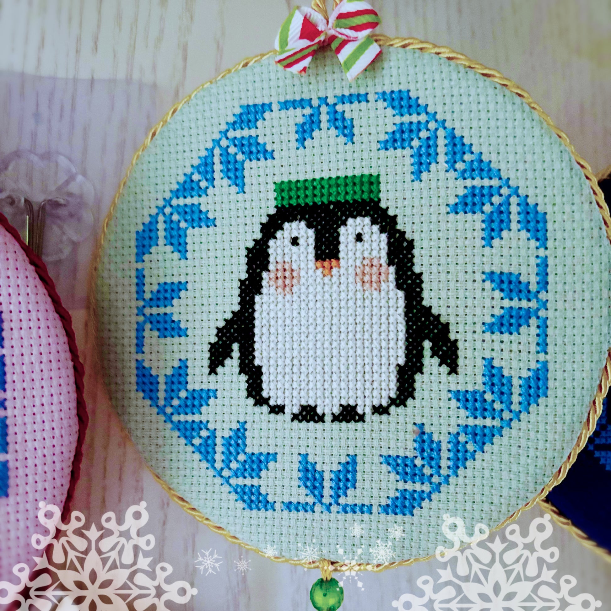 Cross-stitched penguins design on a fabric hoop with a decorative bow.