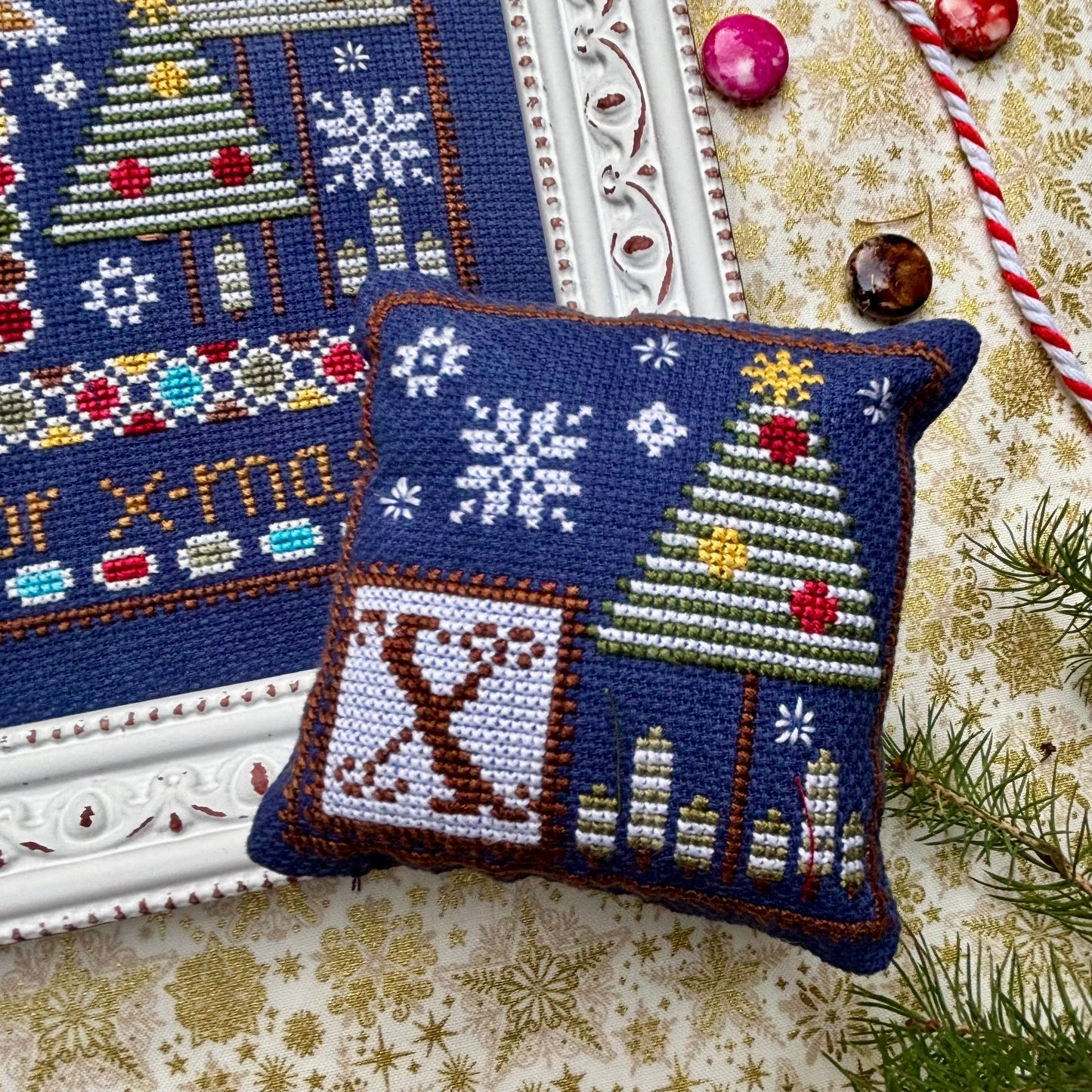 Decorative cross-stitched pillow with Christmas design on a textured surface.