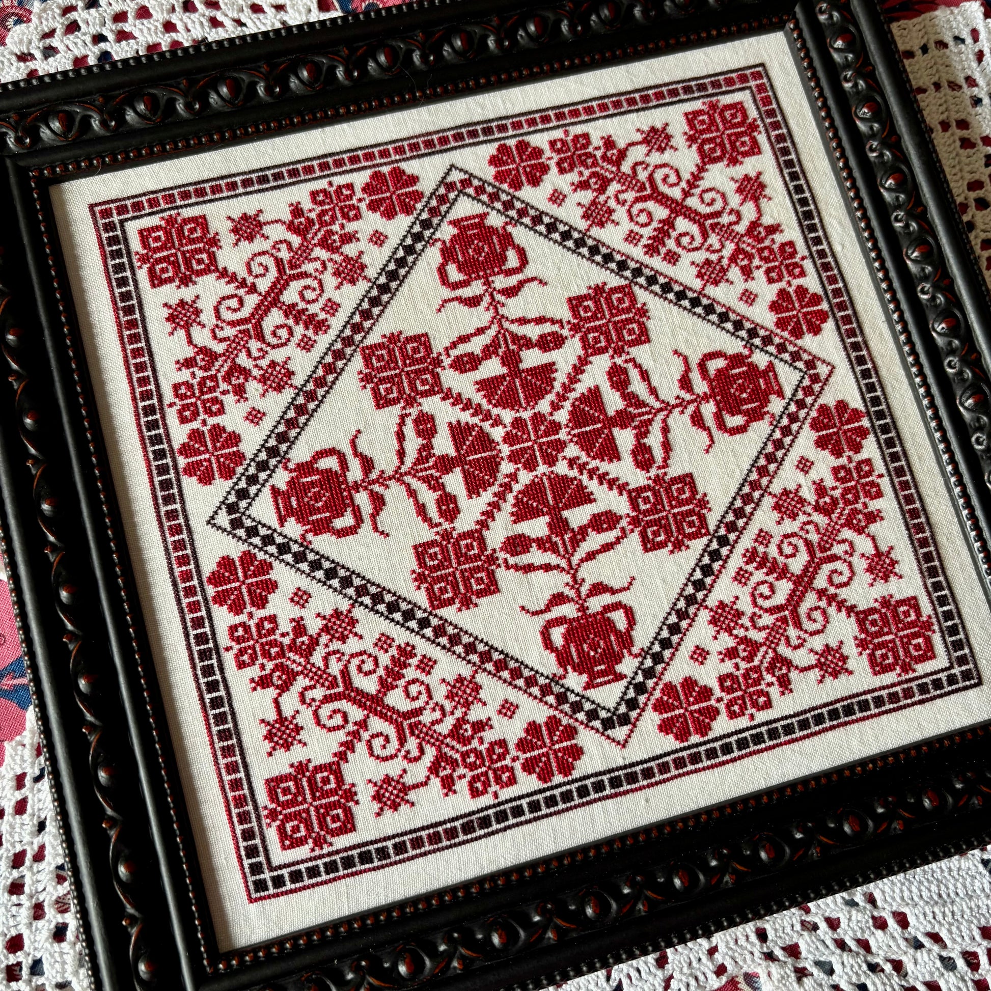 Framed cross-stitched piece with red floral patterns on white fabric