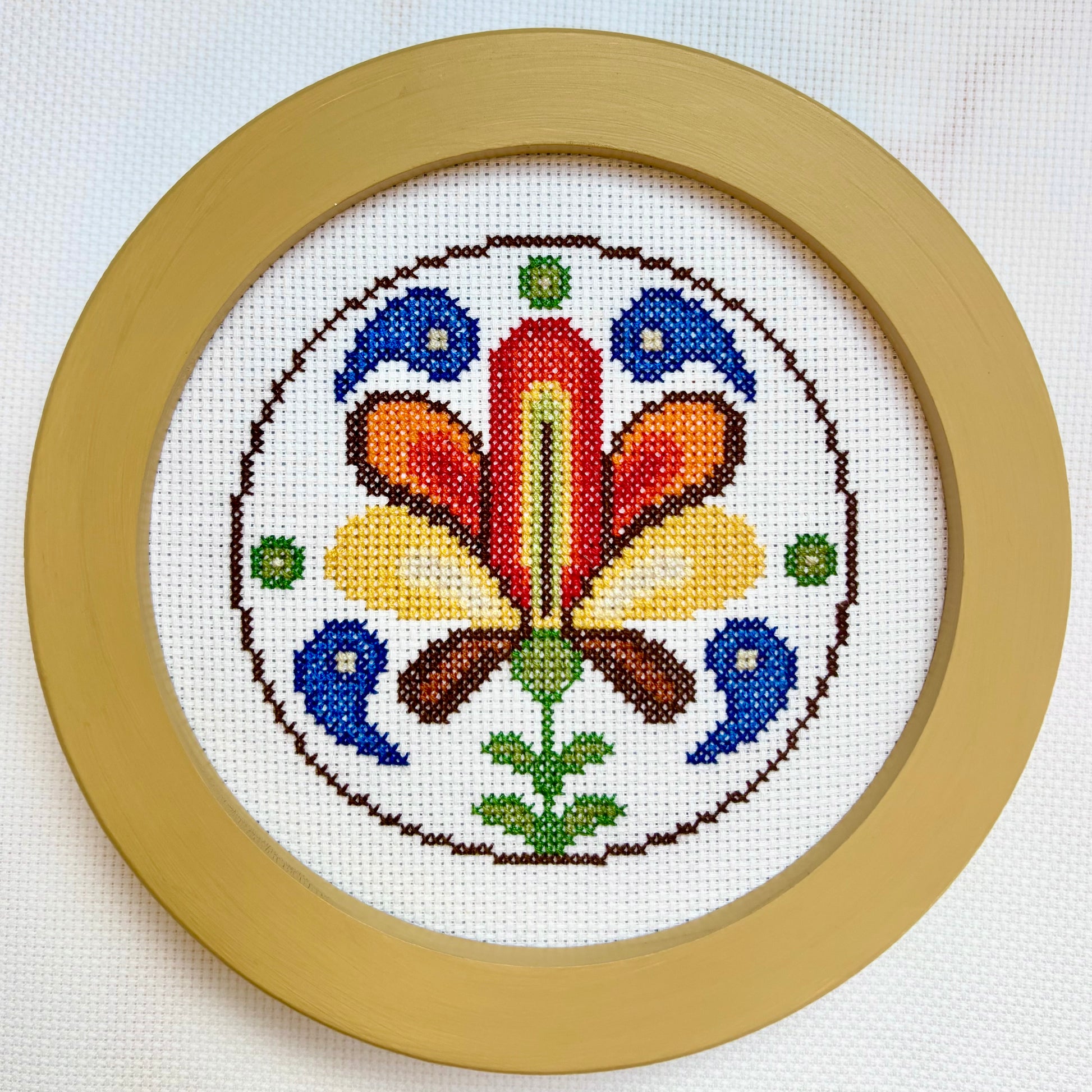 Cross-stitched design with colorful floral pattern in a wooden frame on a white background