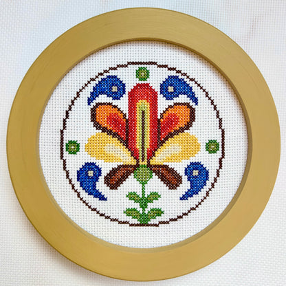 Cross-stitched design with colorful floral pattern in a wooden frame on a white background