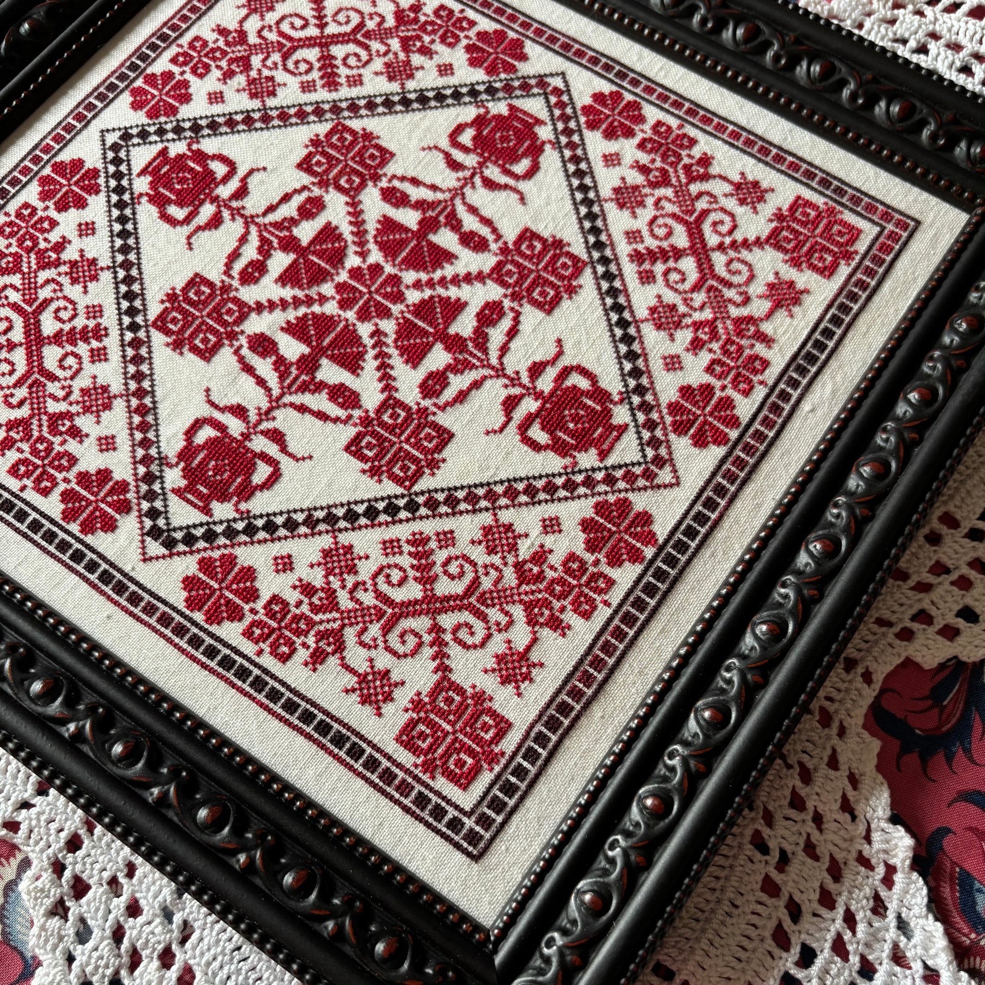Embroidered red floral pattern on a white fabric with a black frame.