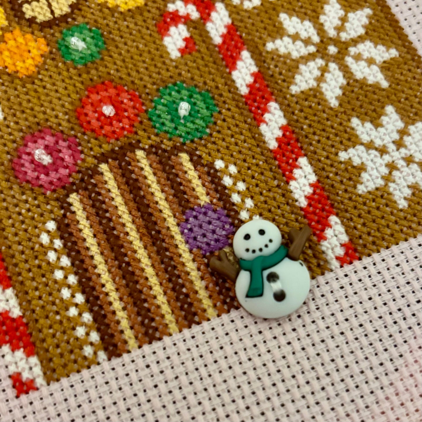 Close-up of a cross-stitched gingerbread house with candy canes and snowflakes.