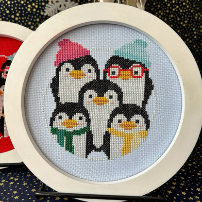 Cross-stitched penguins with accessories in a circular frame on a dark background
