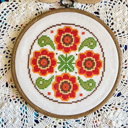 Cross-stitched floral pattern in a wooden hoop on a textured fabric background