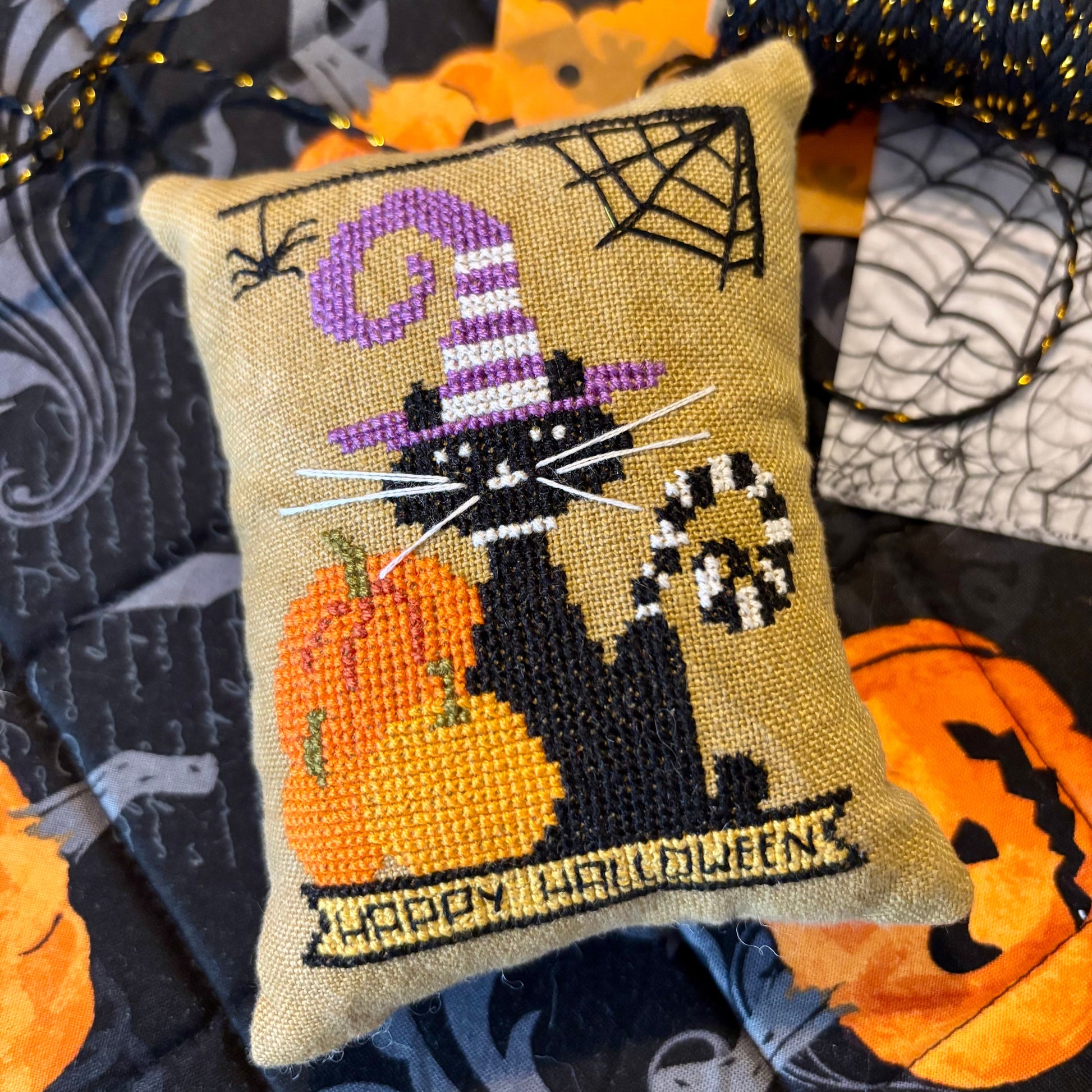 Decorative Halloween pillow with a cat, pumpkin, and candy cane design on a fabric background.