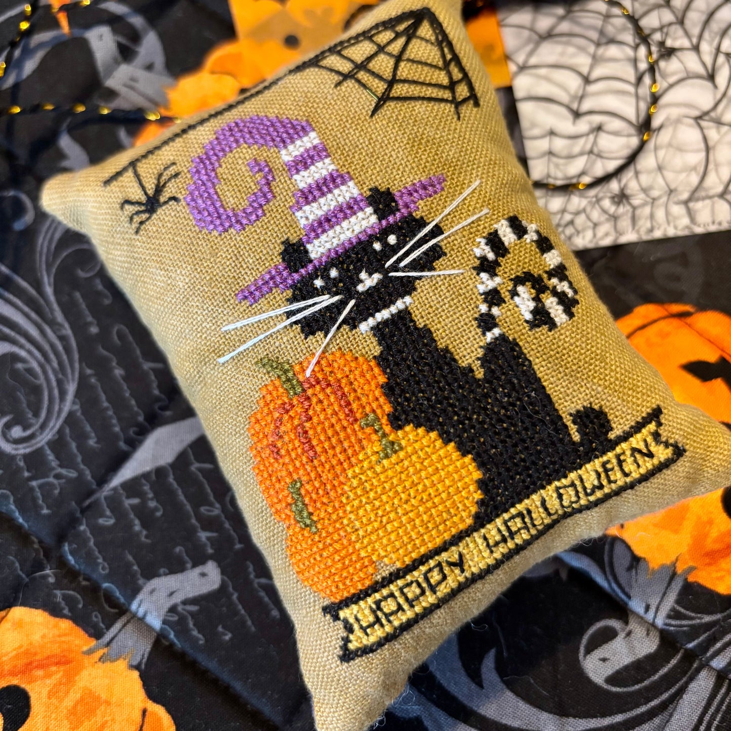Halloween-themed embroidered pillow with a cat, pumpkin, and 'Happy Halloween' text on a fabric background.
