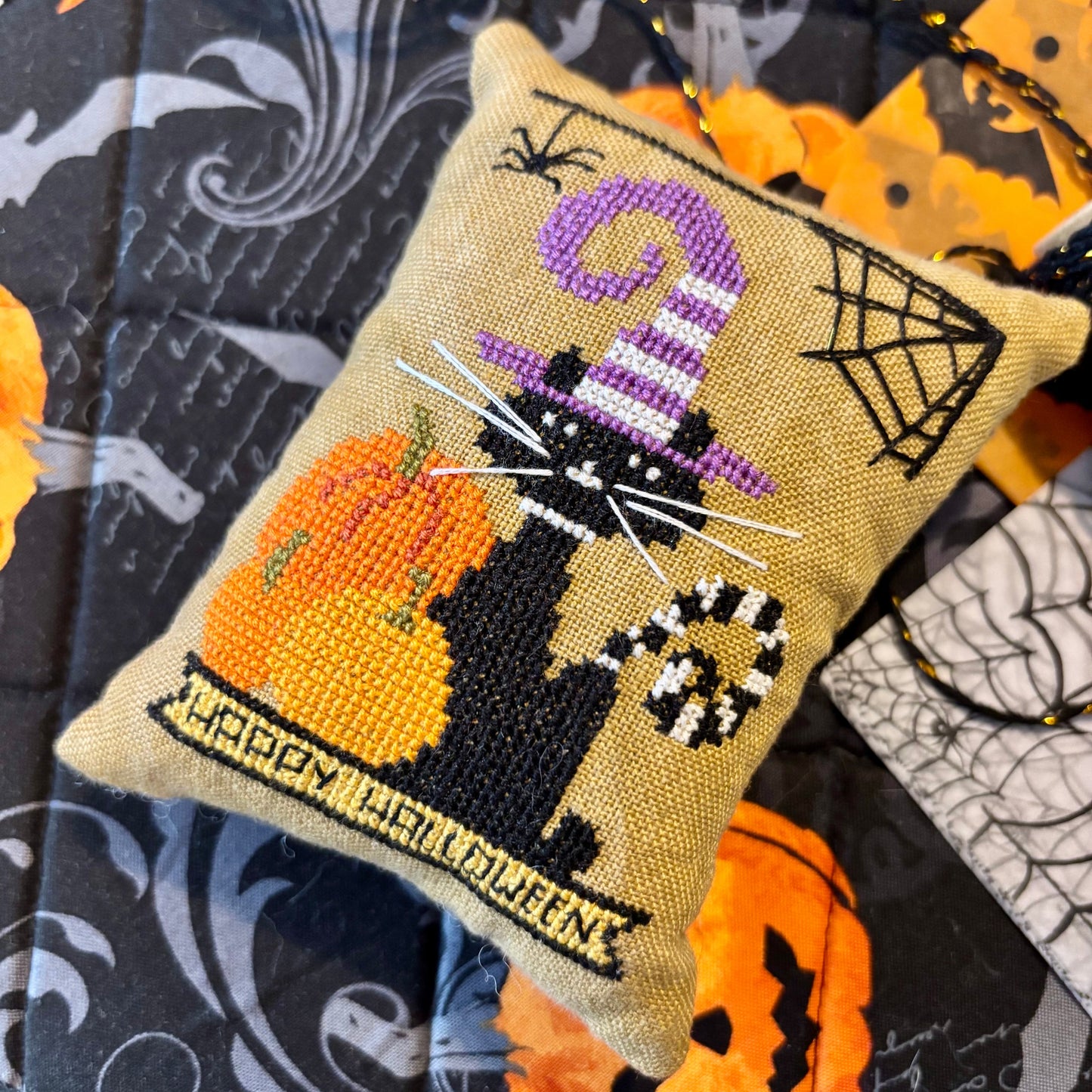 Decorative Halloween pillow with cat, pumpkin, and candy cane design on a patterned background.