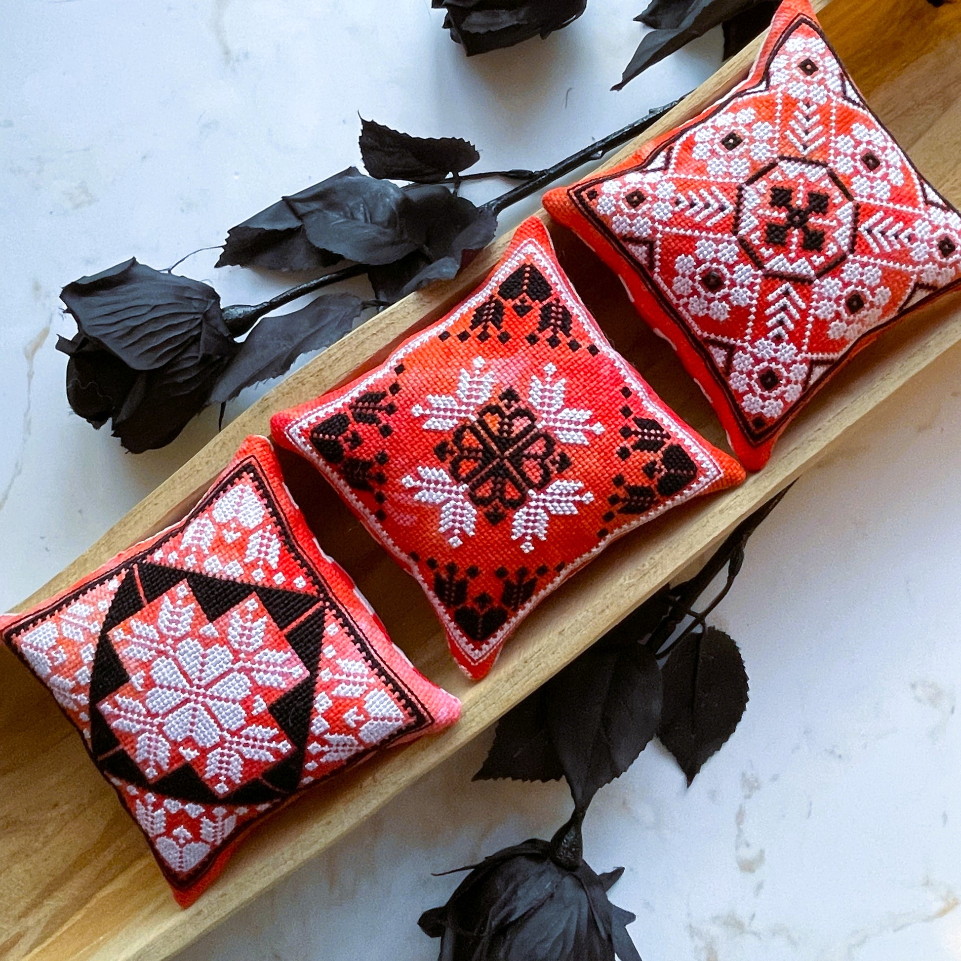 Three red and black embroidered cushions on a wooden surface with black flowers.