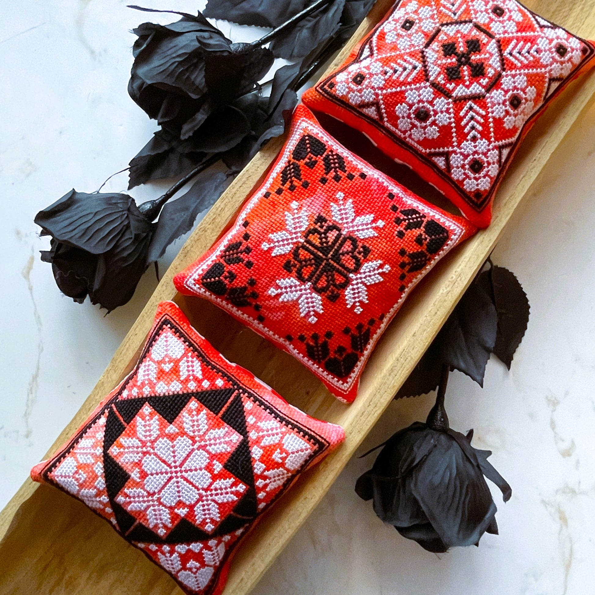 Three red embroidered cushions with black and white patterns on a wooden board.