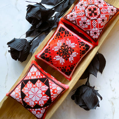 Three red embroidered cushions with black and white patterns on a wooden board.