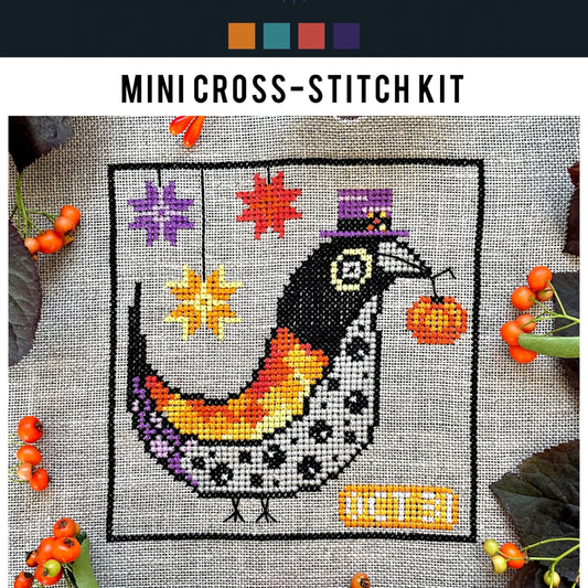 Mini cross-stitch kit with a colorful bird design on fabric surrounded by berries.