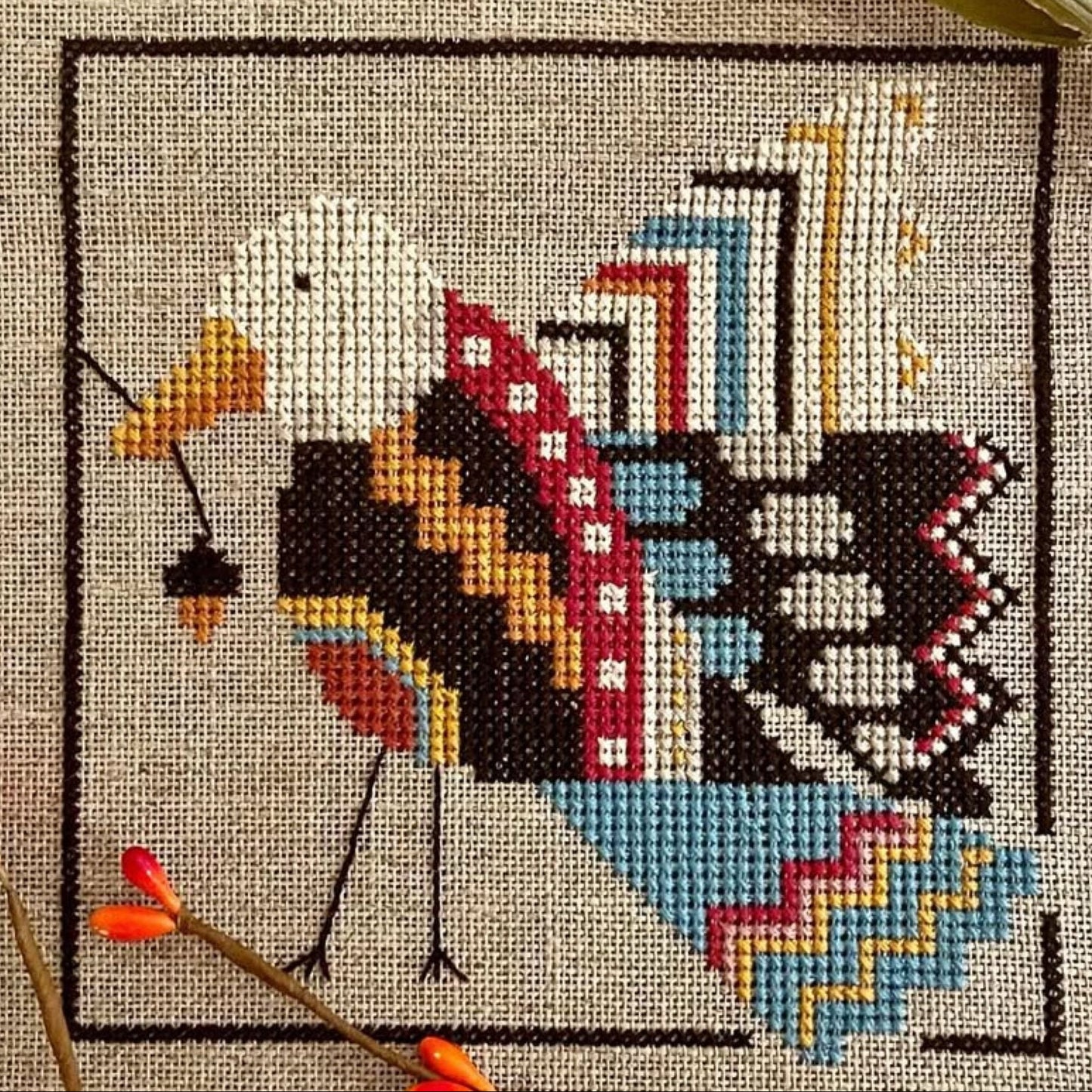Mini cross-stitch kit with a completed design of a bird and acorn on fabric.