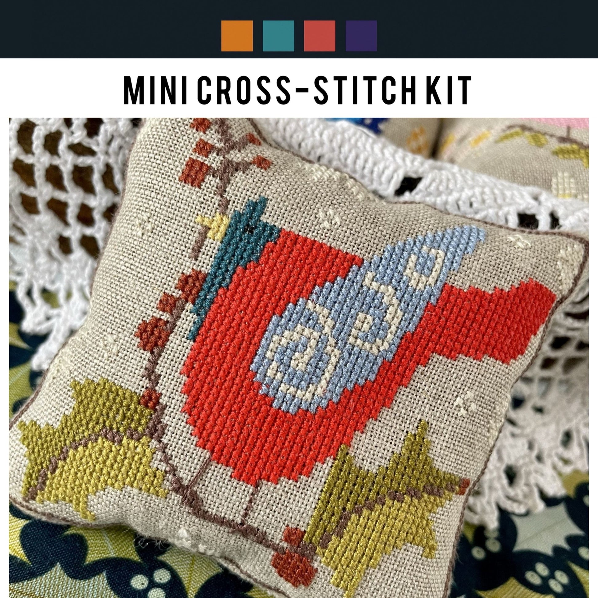 Mini cross-stitch kit with a red and blue bird design on a textured fabric background.