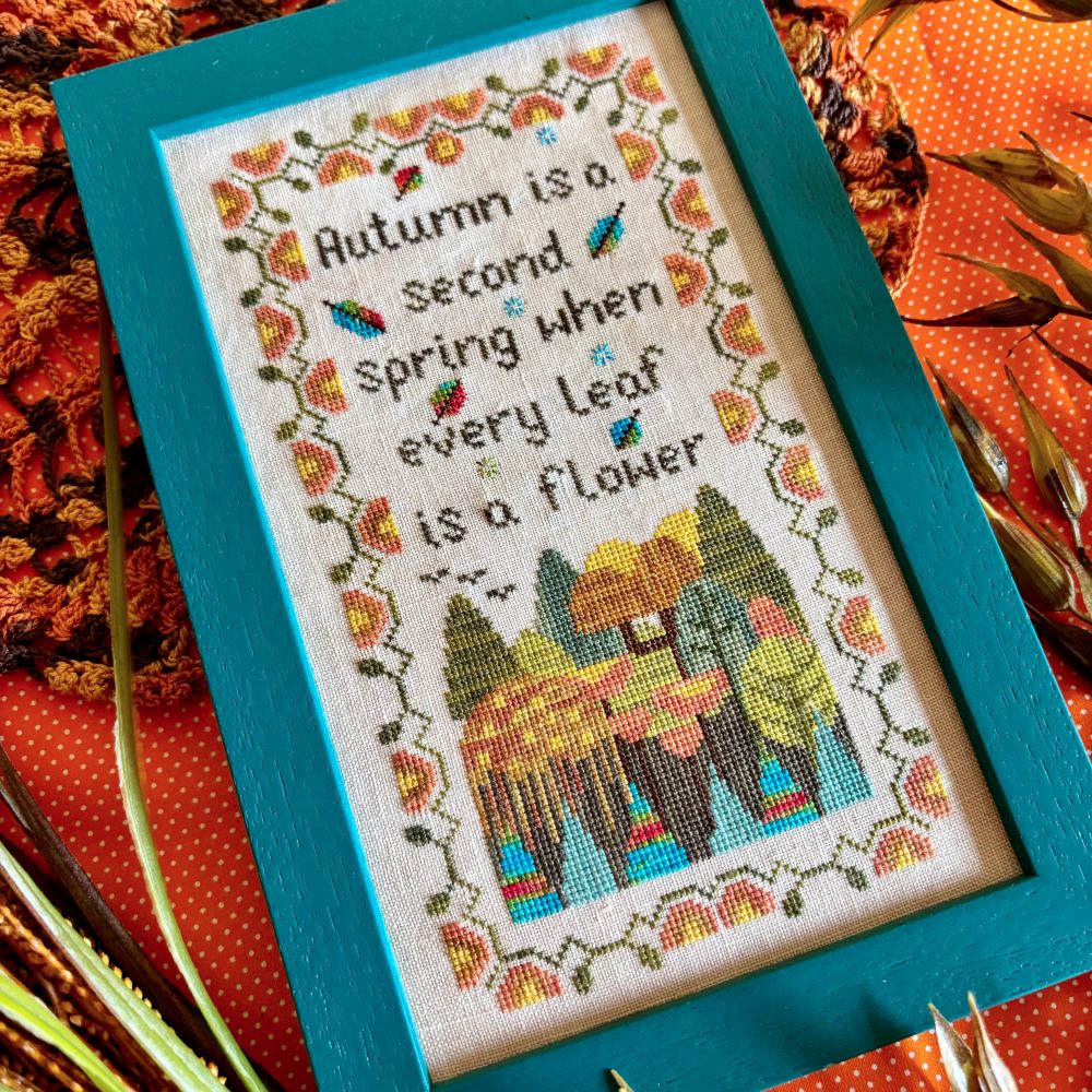 Framed cross-stitched picture with autumn theme and scenic design.