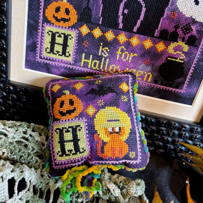 Halloween-themed cross-stitched pillow with pumpkins and the letter 'H'.