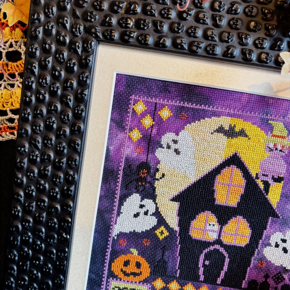 Halloween-themed cross-stitch pattern with a haunted house and pumpkins on a purple background.